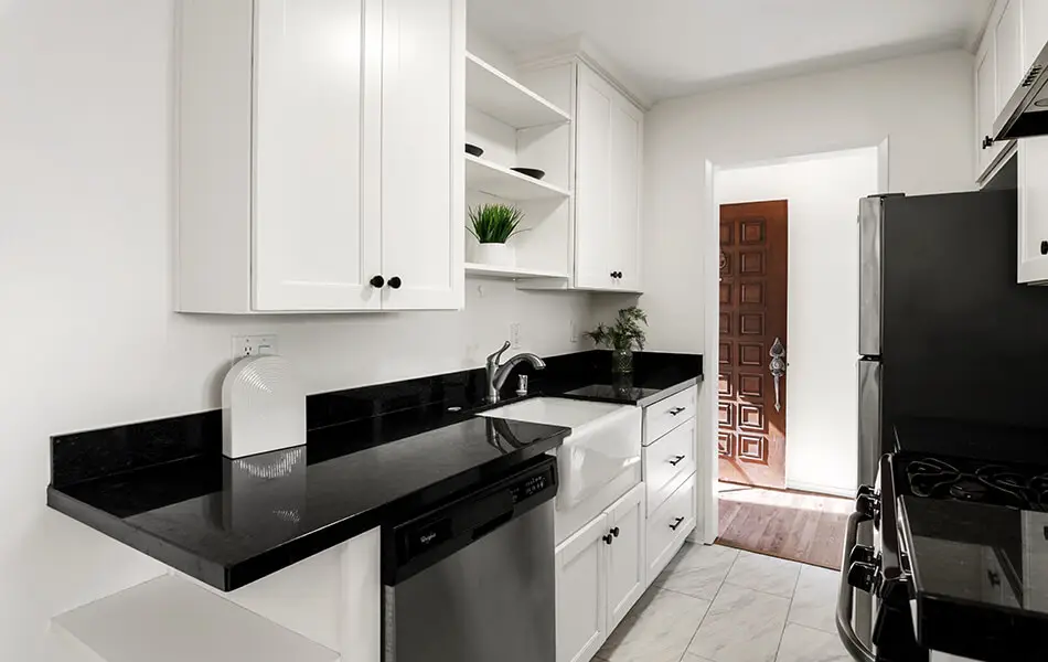 Kitchen with white cabinets black granite counters and dishwasher at 11550 Nebraska Ave West LA condo